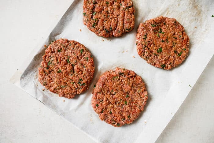 Four ground turkey patties on a baking sheet lined with parchment paper.