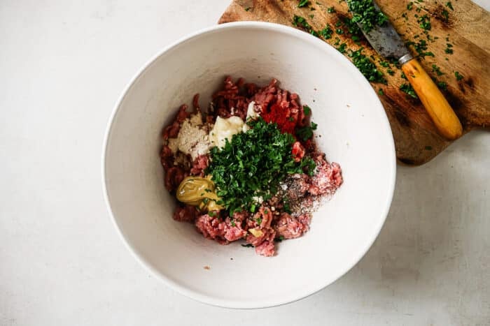 Ground turkey burger ingredients in a large mixing bowl next to a wooden cutting board.