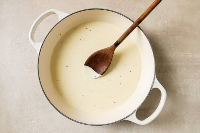 Cream sauce is simmering in the same cast-iron Dutch oven as the garlic.