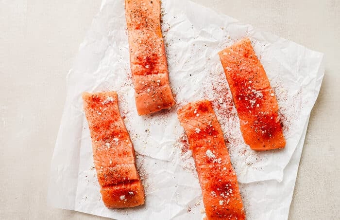 Overhead view of raw, seasoned salmon fillets resting on a paper towel on the kitchen countertop.