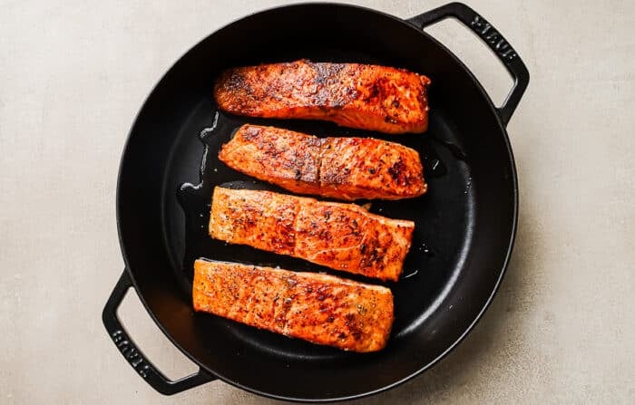 Seared salmon fillets cooking in a cast-iron skillet.