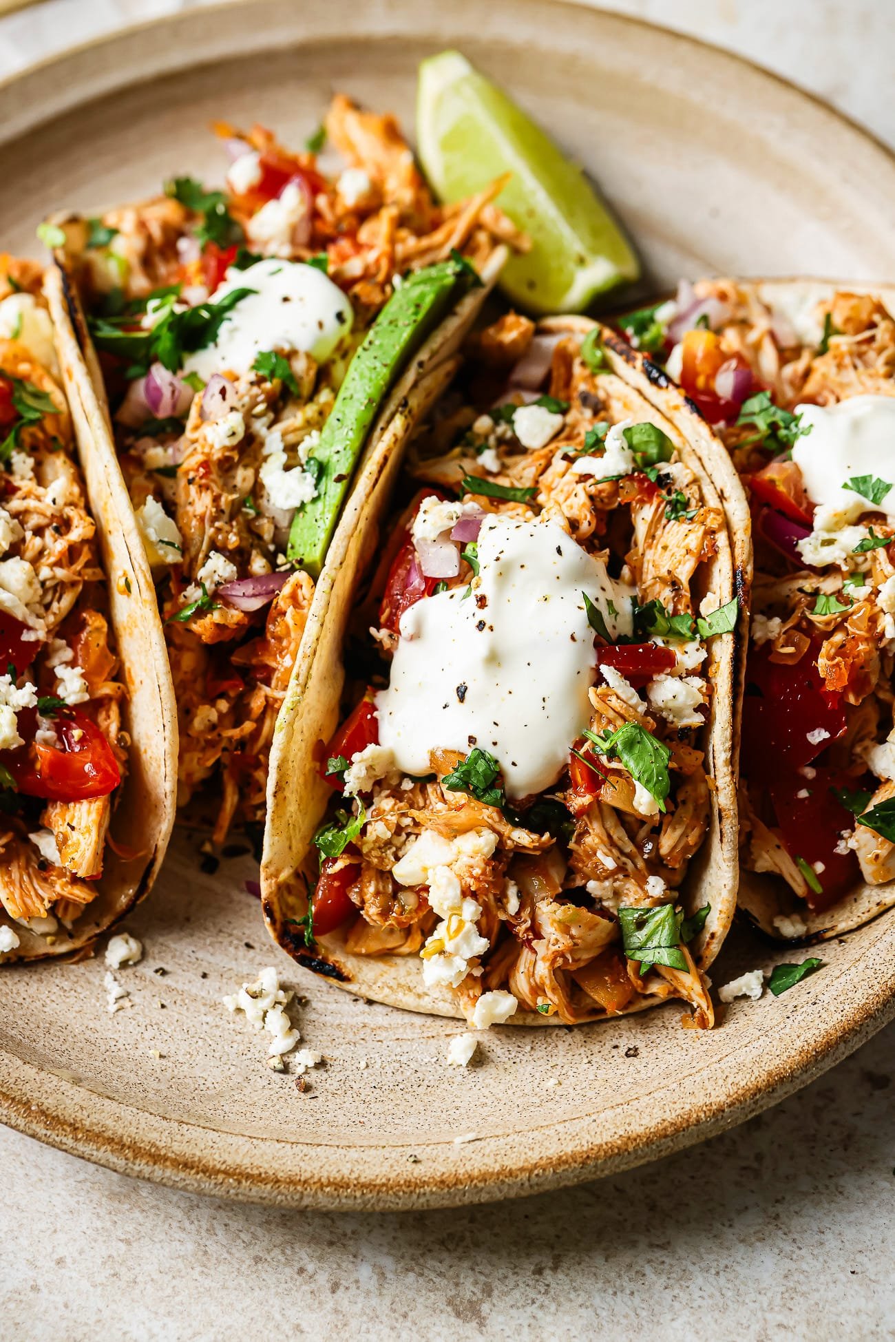 closeup view of shredded chicken tacos served on a plate over a countertop.