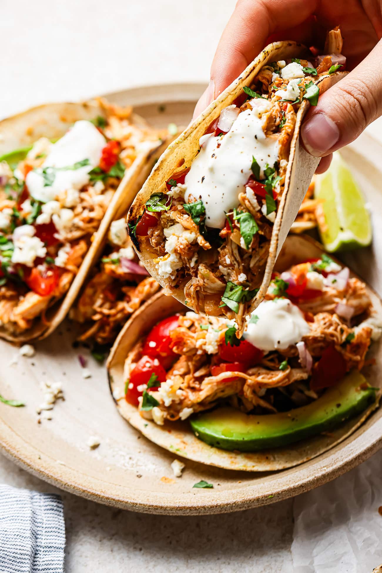 Close-up of shredded chicken tacos with fresh toppings held in hand.