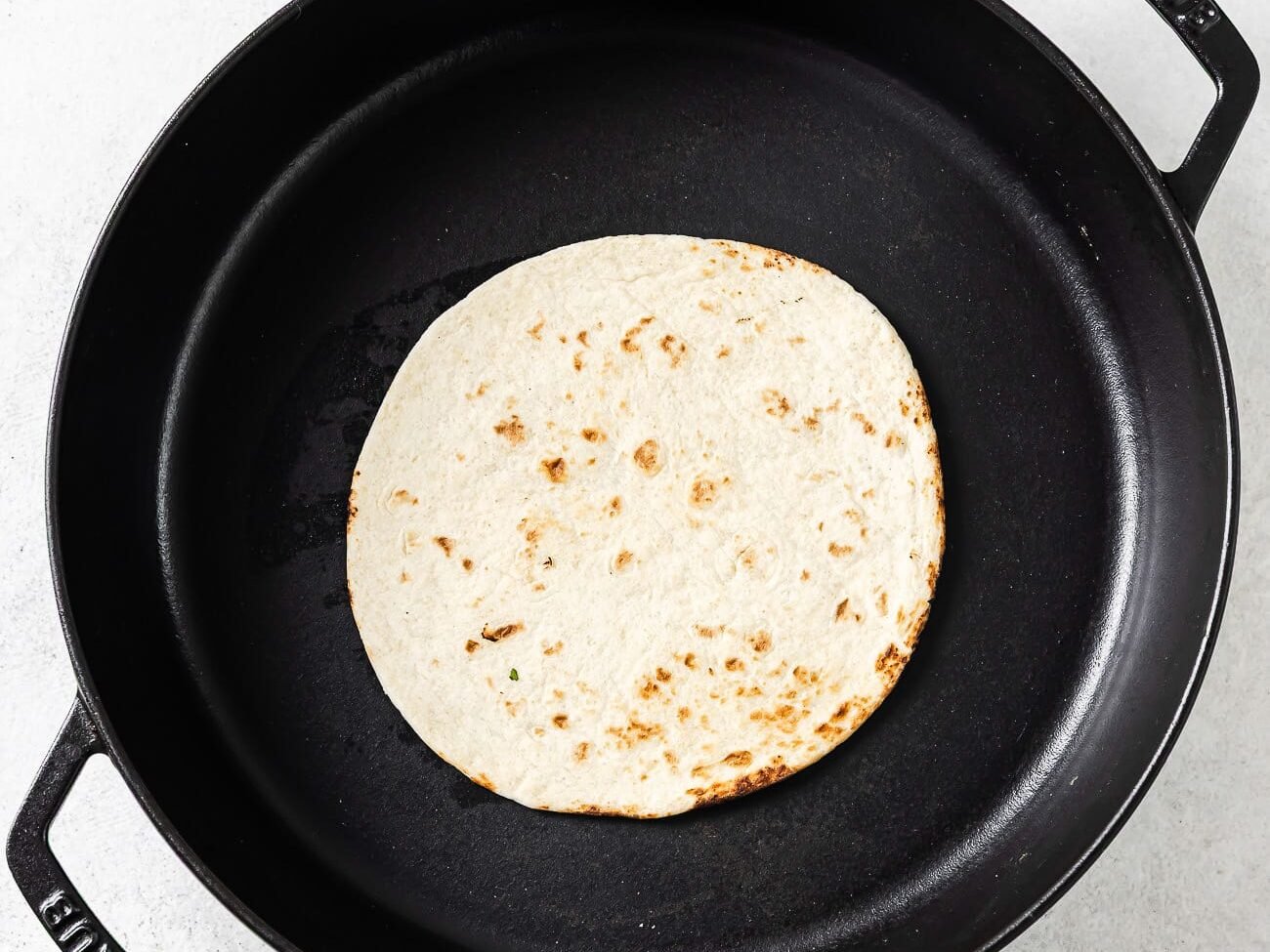 A single flour tortilla is warming in a black cast-iron skillet.