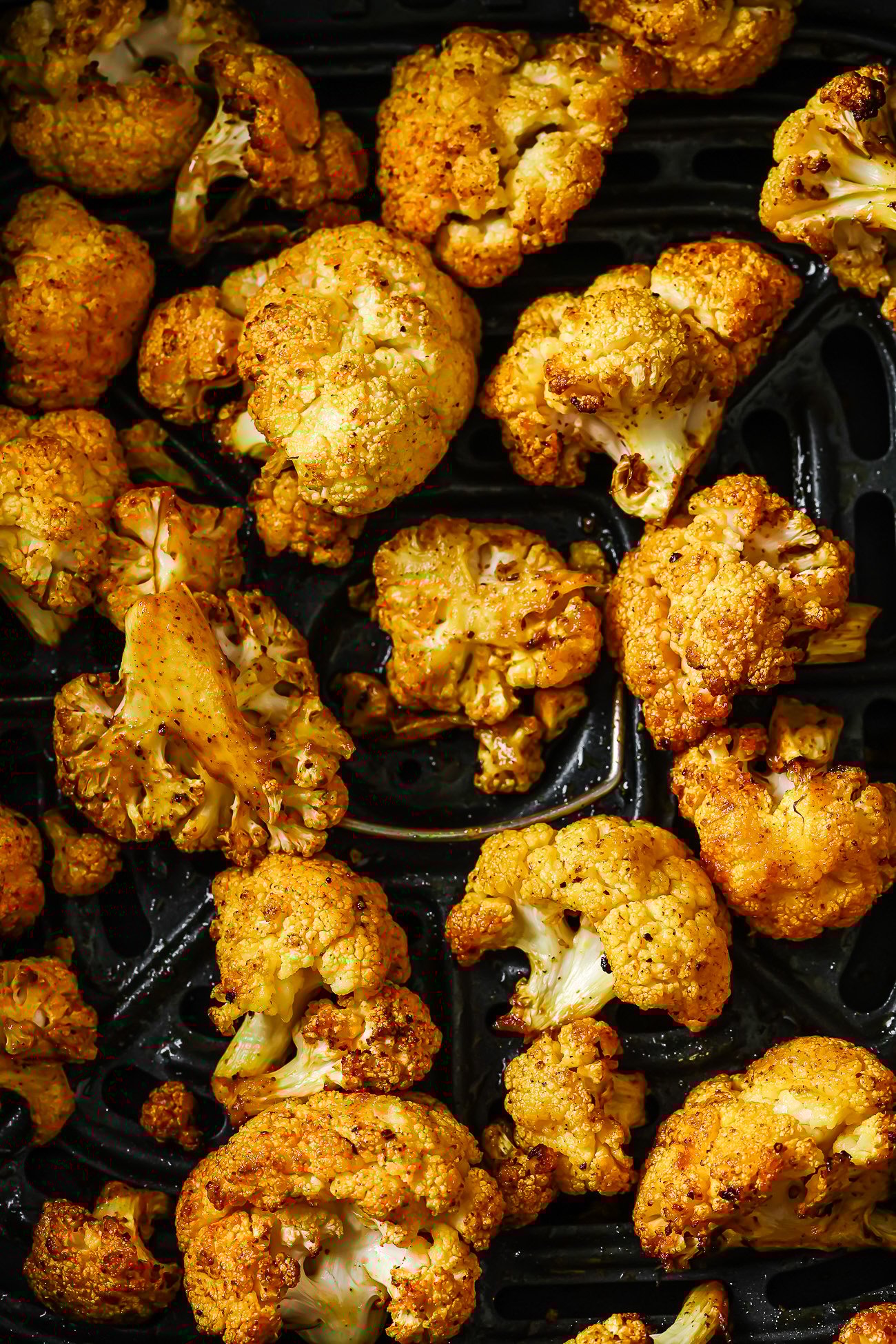 Overhead view of seasoned and cooked cauliflower florets in an air fryer basket.