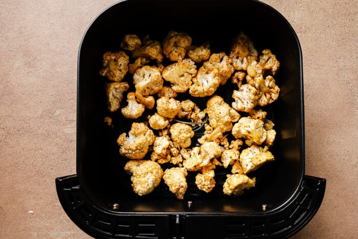 Overhead view of seasoned cauliflower florets in an air fryer basket.