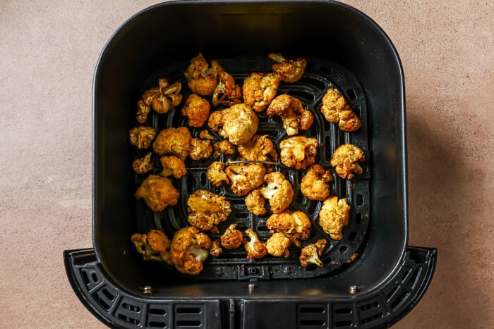 Overhead view of seasoned cooked cauliflower florets in an air fryer basket.
