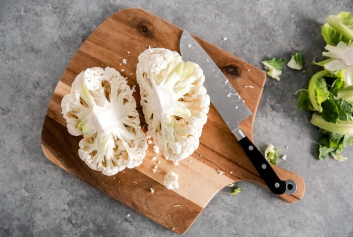 Cauliflower head cut in half on a wooden board.
