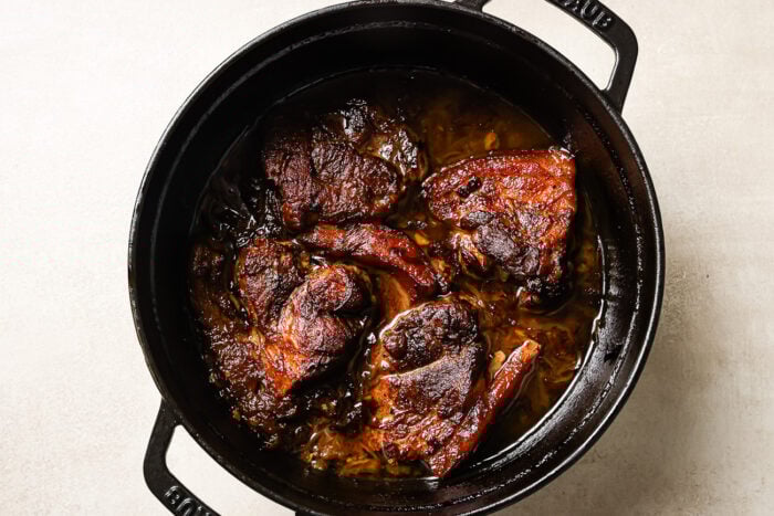 overhead view of apple cider braised pork shoulder in a black Dutch oven pot.