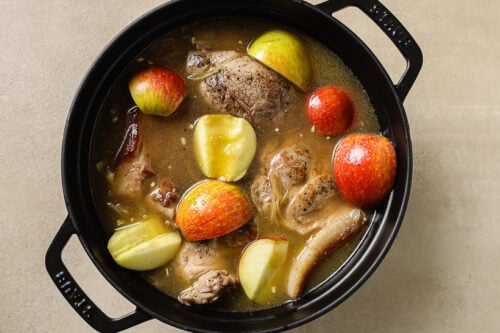 pork shoulder with apple cider and slices of apple in a Dutch oven pot.