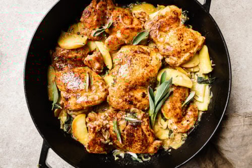 Overhead view of apple cider chicken in a cast iron skillet, coated in a flavorful apple cider sauce.