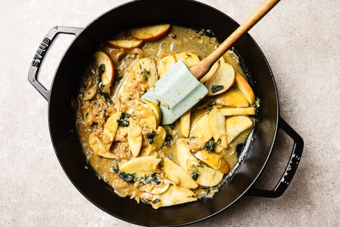 Apple cider sauce with apple slices in a cast iron skillet, reducing to a rich and flavorful glaze.