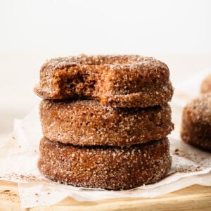 Close-up of three stacked donuts, with the top donut showing a bite taken out, on a wooden surface.