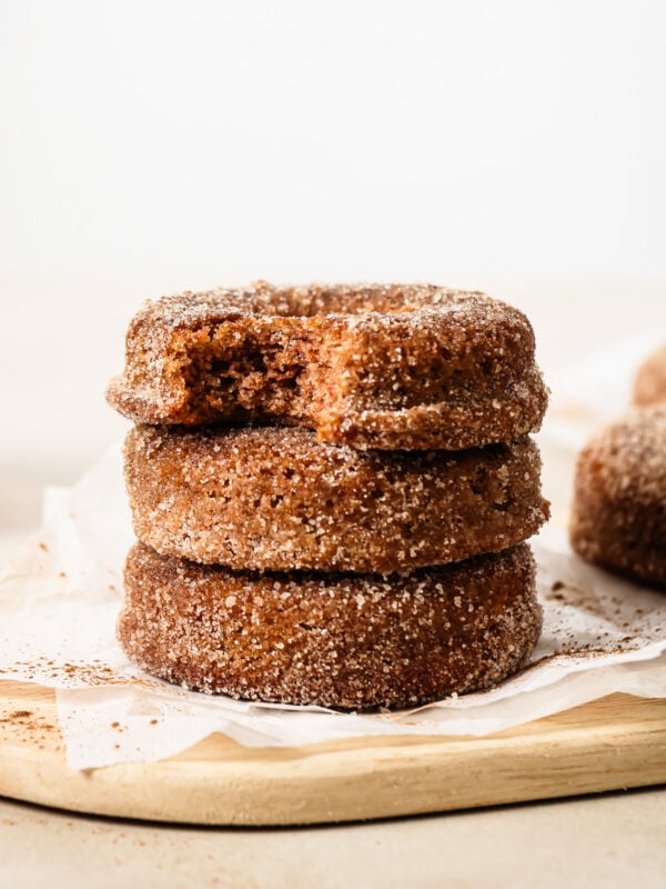 Close-up of three stacked donuts, with the top donut showing a bite taken out, on a wooden surface.