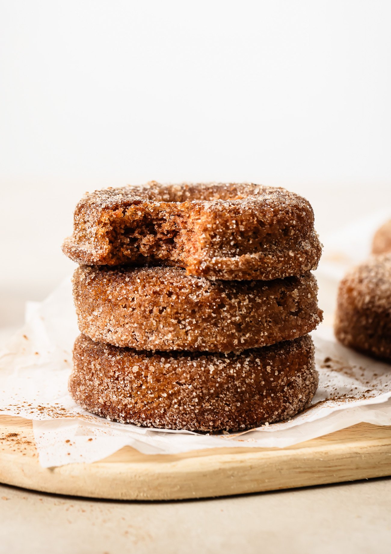 Close-up of three stacked donuts, with the top donut showing a bite taken out, on a wooden surface.