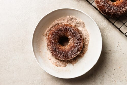 Freshly baked donut on a plate with sugar for coating or rolling.