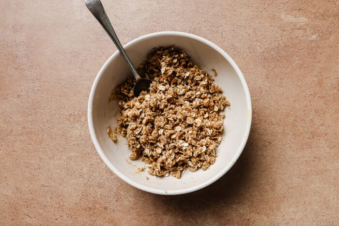 Almond flour, rolled oats, and sugar mixed in a white bowl to create a crunchy apple crisp topping.