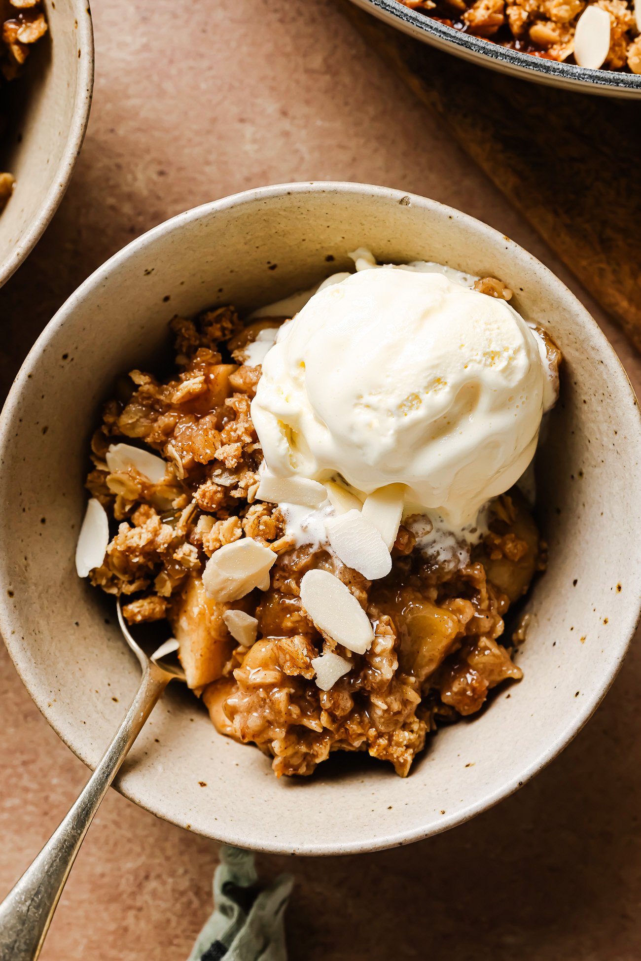 Gluten-free apple crisp in a white bowl topped with creamy vanilla ice cream for a cozy dessert.