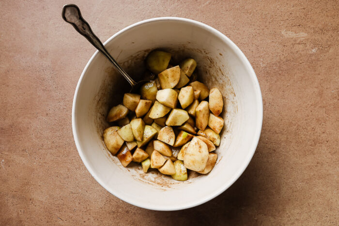 Diced and peeled apples mixed with warm spices in a white bowl, ready for baking.