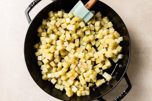 Overhead view of diced raw potatoes in a cast-iron skillet, ready for cooking.