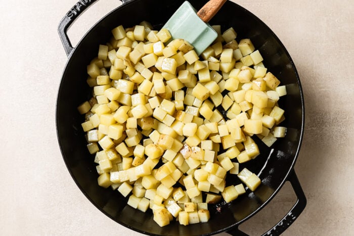 Overhead view of diced raw potatoes in a cast-iron skillet, ready for cooking.