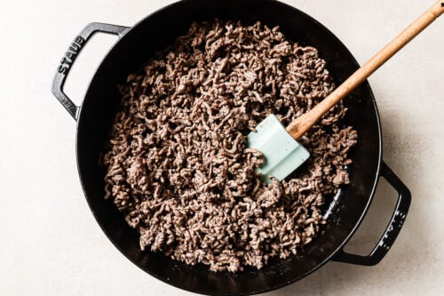 Overhead view of cooked ground beef in a cast-iron skillet, ready to be mixed with vegetables or potatoes.