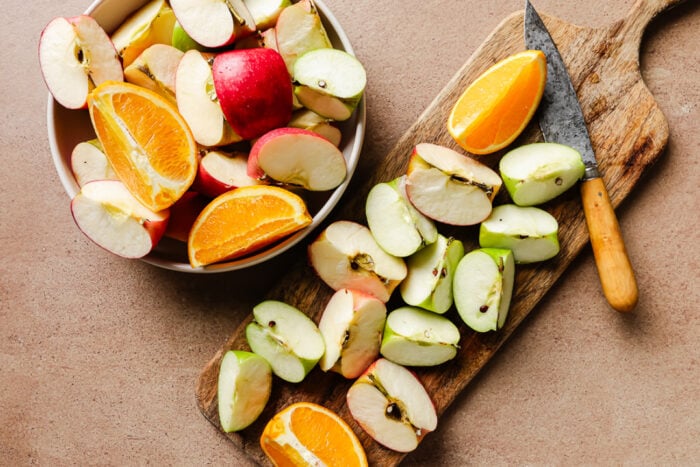 Diced apples and oranges on a wooden cutting board on a kitchen countertop.