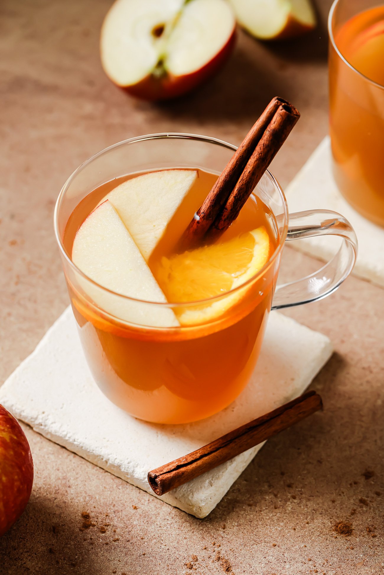 Cup of slow cooker apple cider garnished with a cinnamon stick, apple slices, and orange slices.