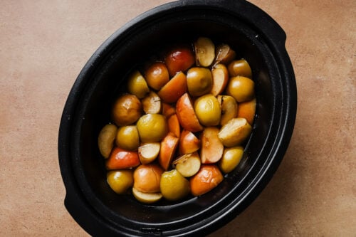 Mashed cooked apples and oranges inside a slow cooker.