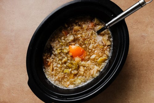 Mashed cooked apples and oranges inside a slow cooker.