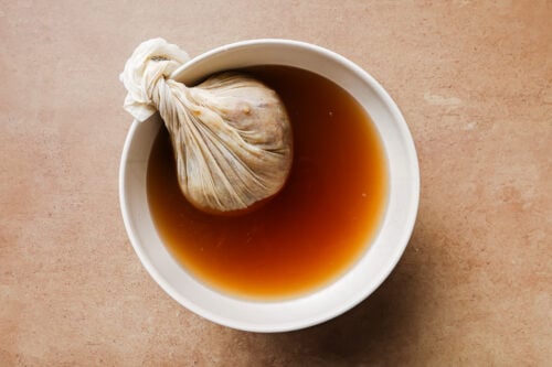 Cheesecloth placed over a large bowl of homemade apple cider.