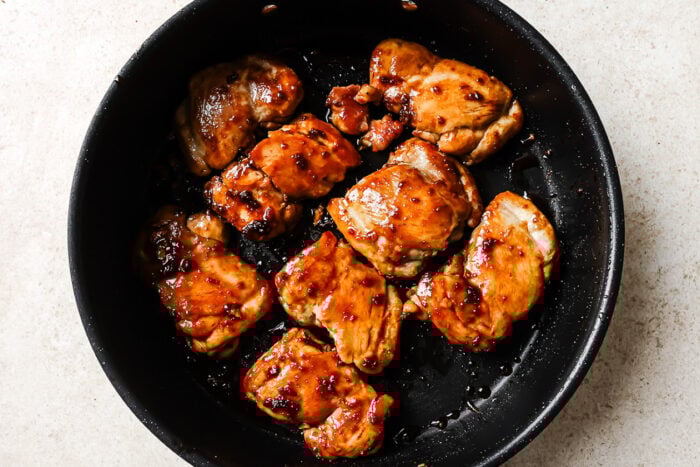 Honey garlic chicken thighs sizzling in a cast iron skillet, glazed with a sweet and savory sauce.
