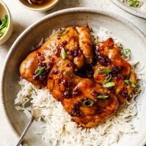 Close-up of honey garlic chicken thighs served over rice in a white bowl.