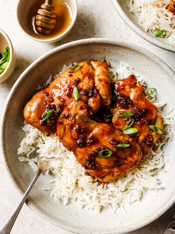 Close-up of honey garlic chicken thighs served over rice in a white bowl.