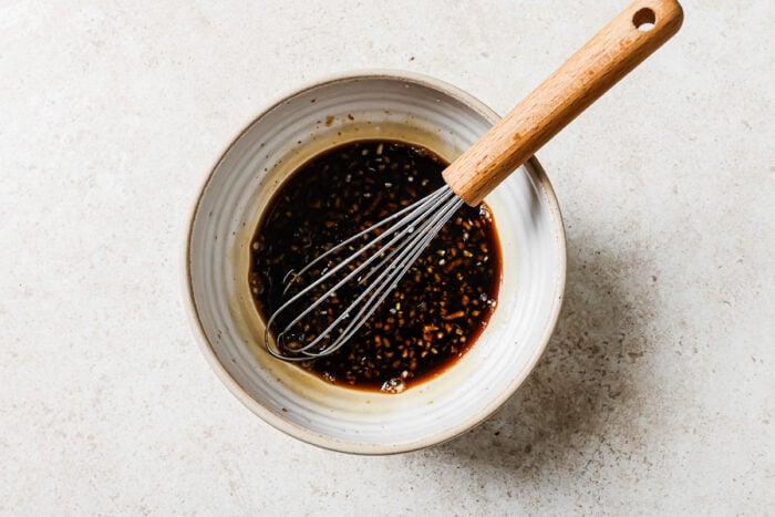 Homemade honey garlic sauce in a white bowl with a whisk, ready for glazing chicken.