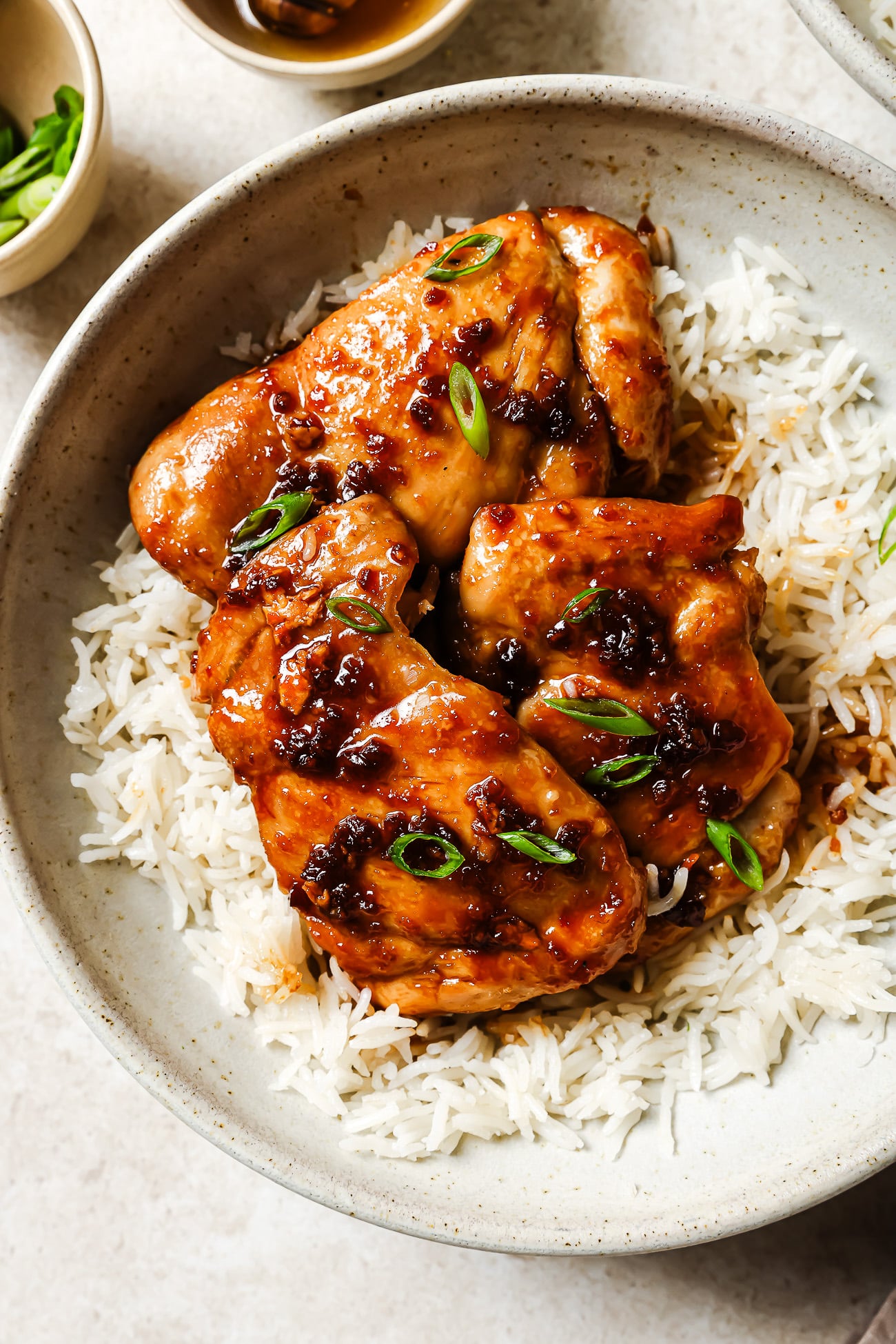 Close-up of honey garlic chicken thighs served over rice in a white bowl.