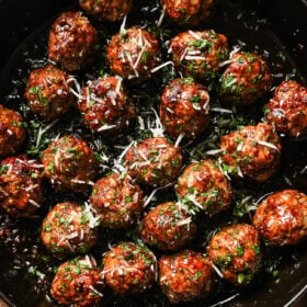 A pan filled with Honey Garlic Meatballs, glazed to perfection and garnished with chopped herbs and grated cheese.