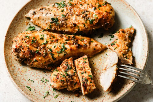 Slow cooker chicken breasts served on a plate with a fork.
