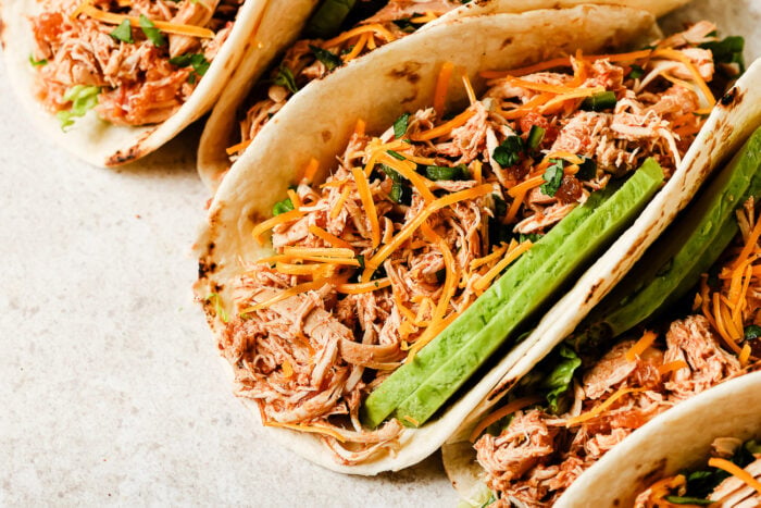 Close-up view of slow cooker chicken tacos filled with shredded chicken, salsa, and fresh toppings.