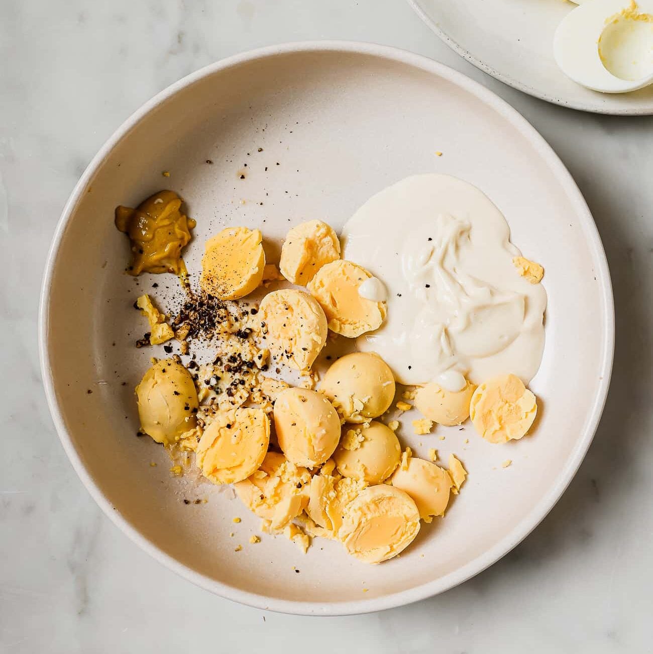 egg yolks and all the ingredients to make deviled egg on a white plate