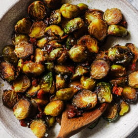 Overhead view of maple bacon Brussels sprouts in a white platter, coated in a sweet maple glaze with crispy bacon pieces.