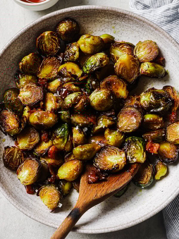 Overhead view of maple bacon Brussels sprouts in a white platter, coated in a sweet maple glaze with crispy bacon pieces.