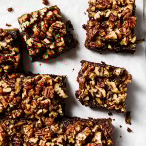 Overhead view of pecan pie brownies cut into squares on parchment paper, featuring a gooey chocolate base and caramelized pecan topping.