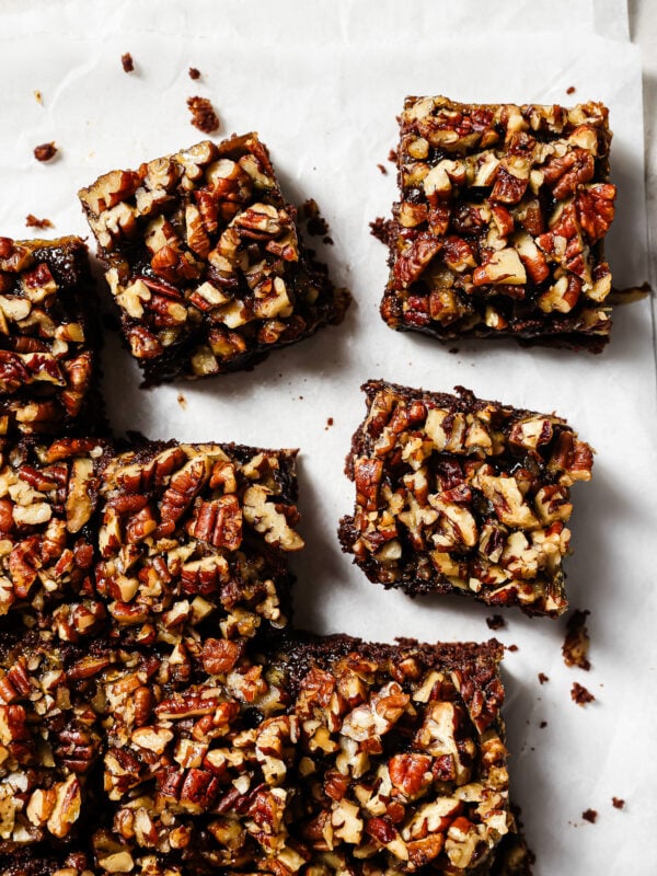 Overhead view of pecan pie brownies cut into squares on parchment paper, featuring a gooey chocolate base and caramelized pecan topping.