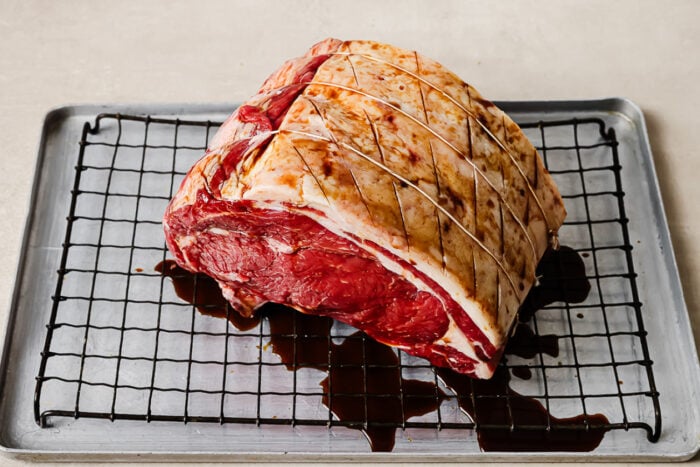 Raw prime rib roast on a wire rack being coated with Worcestershire sauce for the reverse sear prime rib recipe.