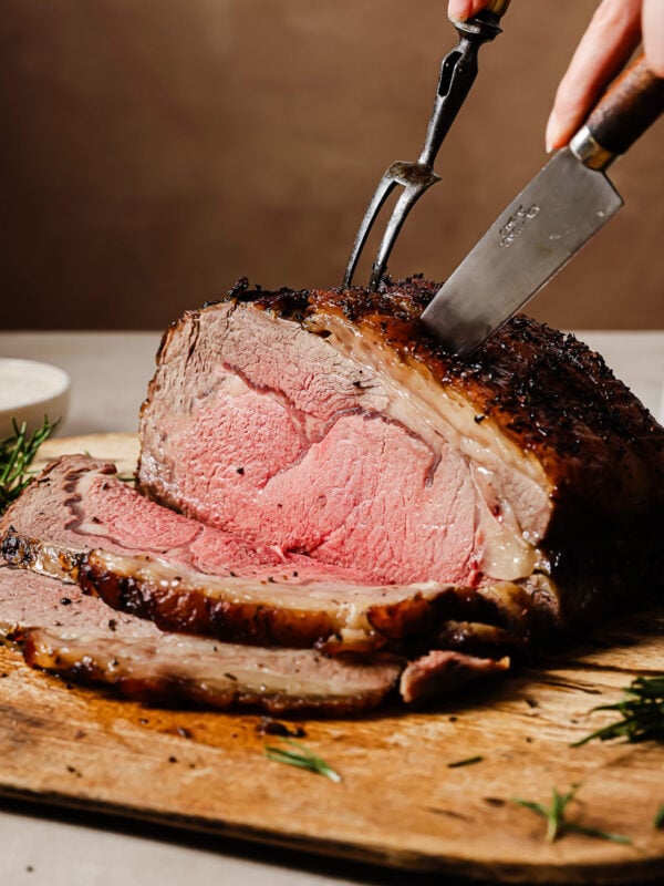 Reverse sear prime rib being sliced on a wooden cutting board, showing its juicy and perfectly cooked interior.
