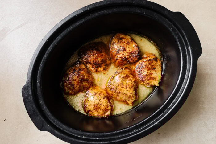 overhead view of uncooked rice and chicken thighs in a slow cooker pot.