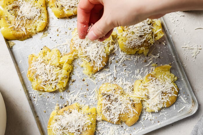 Hand adding grated Parmesan cheese on top of potatoes.