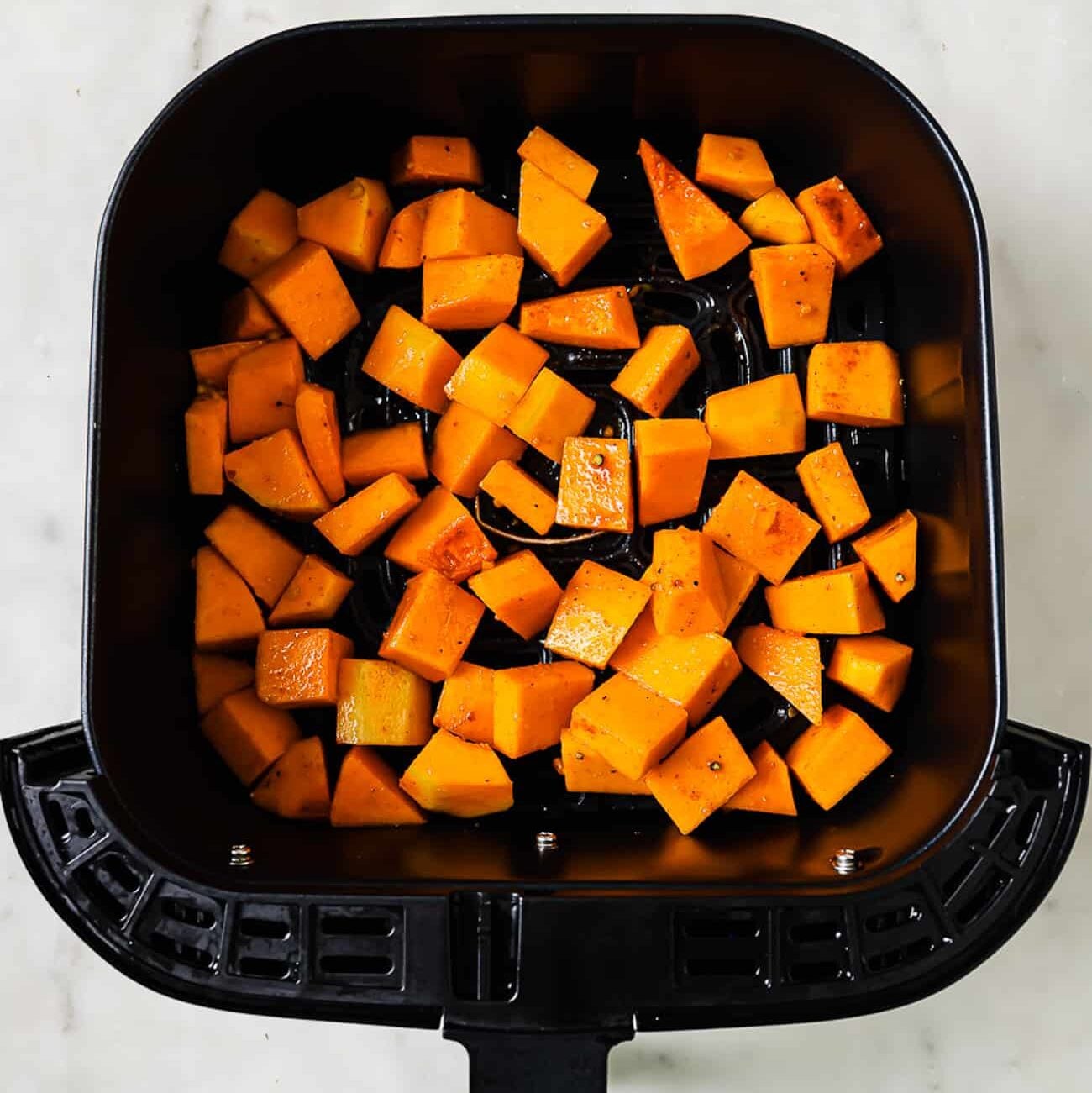 An overhead view of butternut squash in an air fryer basket.