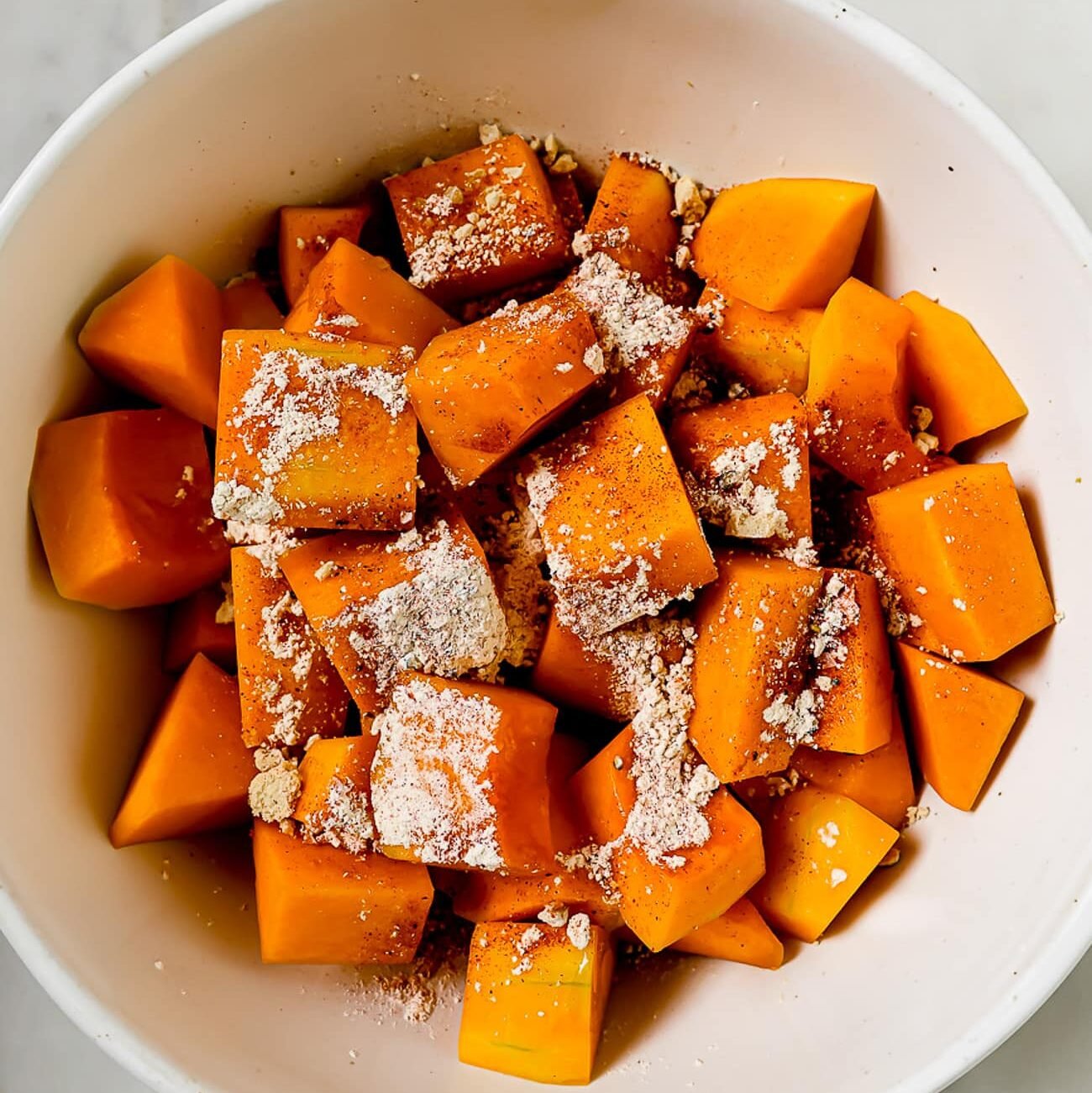 An overhead view of butternut squash and seasonings in a bowl.